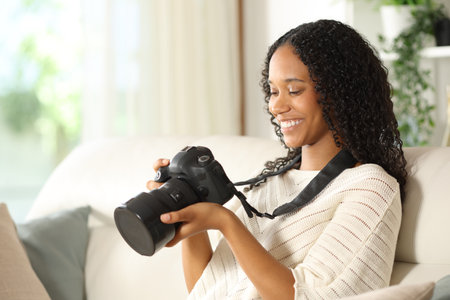 Happy black photographer checking camera sitting on a couch at home