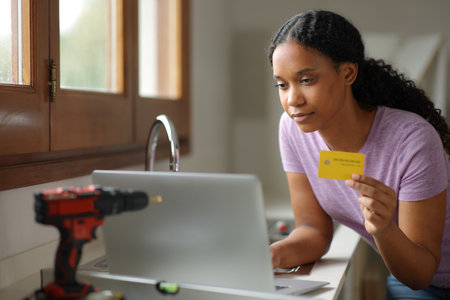 Black woman renovating house in the kitchen buying online with laptop and credit cardの写真素材