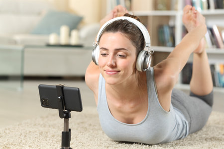 Woman wearing headphone watching and listening online yoga class on the floor at homeの写真素材