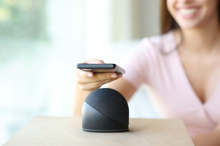 Close up of a happy woman pairing smart speaker with cell phone at homeの写真素材