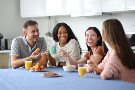 Happy interracial roommates and friends talking and laughing in the kitchen at breakfastの写真素材