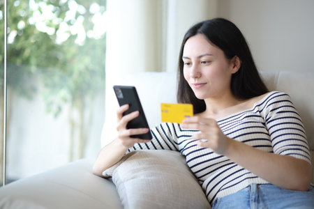 Serious asian woman buying online with credit card and smart phone at home