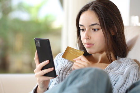 Serious woman buying online using credit card and smart phone at homeの写真素材