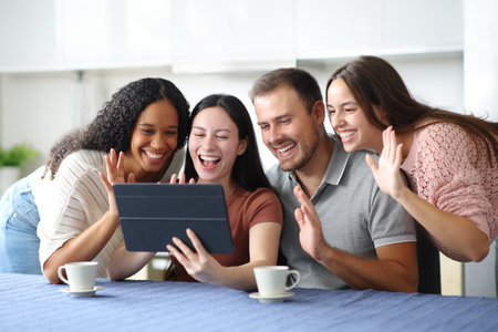 Happy friends greeting having video call on tablet in the kitchen at homeの写真素材