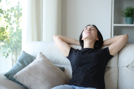 Front view portrait of a relaxed asian woman resting on a couch at homeの写真素材