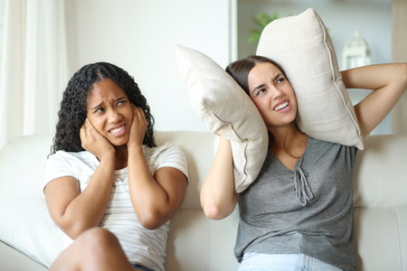 Interracial lesbian couple or roommates annoyed by neighbor noise covering ears with pillows at homeの写真素材