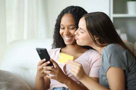 Affectionate interracial lesbian couple buying online with credit card and cell phone at homeの写真素材