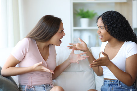 Two angry interracial friends arguing sitting at homeの写真素材