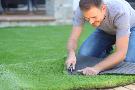 Happy man installing artificial lawn cutting a piece in the garden at homeの写真素材