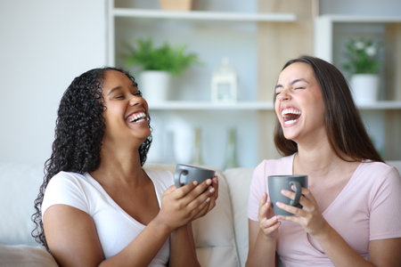 Funny friends talking and laughing drinking coffee at homeの写真素材