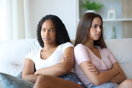 Angry lesbian couple or friends ignoring each other sitting on a couch at homeの写真素材