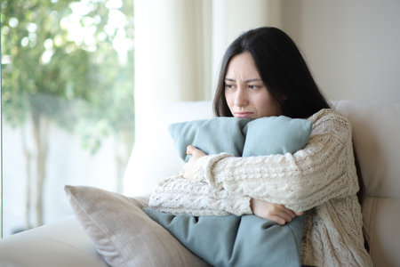 Sad asian woman complaining hugging pillow sitting on a couch at homeの写真素材
