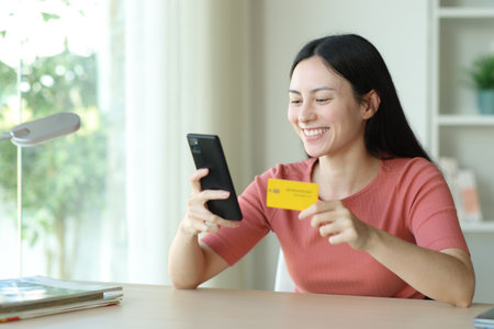 Happy asian woman buying online with credit card and phone on a desk at homeの写真素材