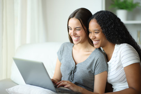 Funny interracial couple checking laptop sitting on a couch at homeの写真素材