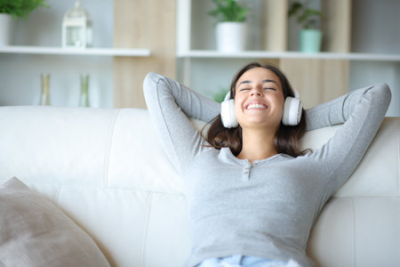 Happy woman at home listening music with headphone resting sitting on a couchの写真素材
