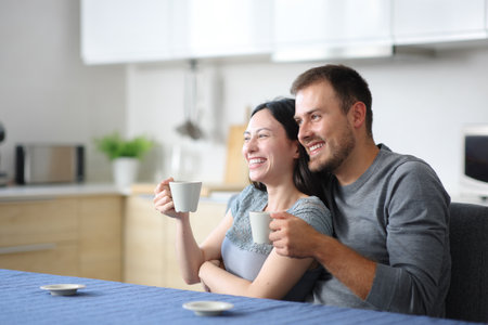 Happy interracial couple drinking coffee and relaxing in the kitchen at homeの写真素材