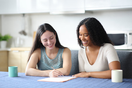 Happy interracial roommates signing paper contract in the kitchen at homeの写真素材