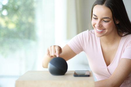 Happy woman setting smart speaker pushing button at homeの写真素材