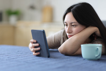 Serious asian woman reading ebook in the kitchen at home