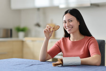 Happy woman eating cookies looking at you in the kitchen at homeの写真素材