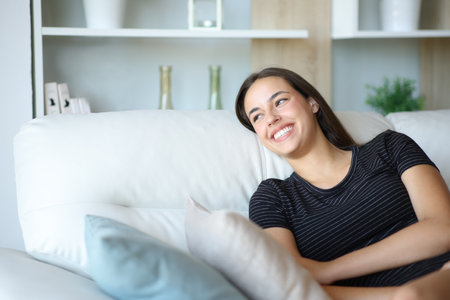 Happy woman laughing sitting on a sofa looking at side at homeの写真素材