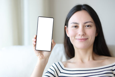 Front view of an asian woman showing blank phone screen at homeの写真素材