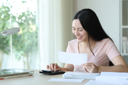 Asian woman using calculator holding bills on a desk at homeの写真素材