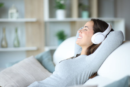 Profile of a happy woman wearing headphone listening audio relaxing sitting on a couch at homeの写真素材