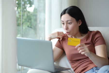 Shocked asian woman buying online with laptop and credit card at homeの写真素材