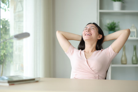 Happy asian woman relaxing sitting on a chair in a room at homeの写真素材