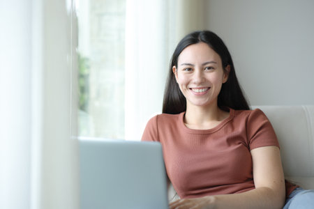 Front view portrait of a happy asian woman with laptop looking at you at homeの写真素材