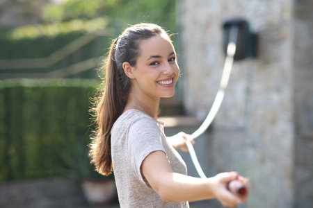 Happy woman unreeling hose pipe looking at you in a garden at home