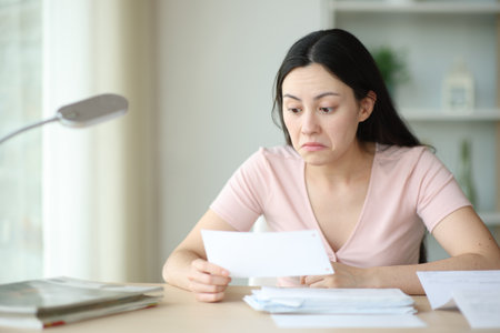 Perplexed asian woman checking bill at homeの写真素材