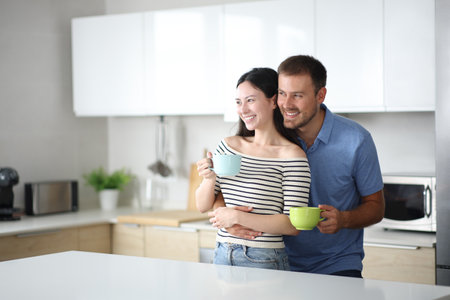 Happy interracial couple contemplating and hugging drinking coffee in the kitchen at homeの写真素材