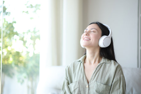 Happy asian woman breathing wearing headphone sitting on a couch at homeの写真素材