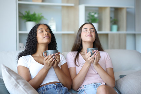 Two friends breathing drinking coffee relaxing sitting on a couch at homeの写真素材