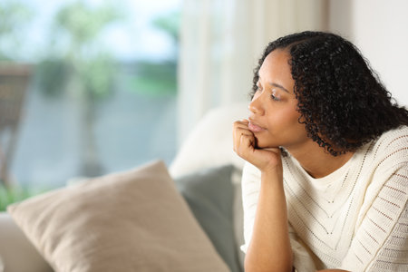 Distracted black woman thinking sitting on a sofa at homeの写真素材