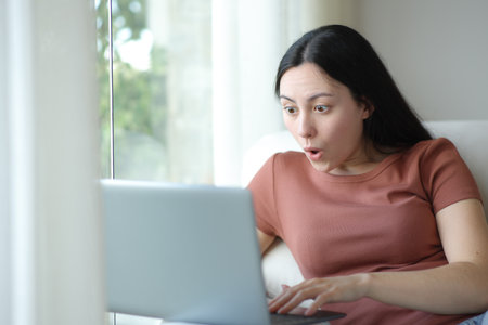Amazed woman using laptop sitting on a couch at homeの写真素材