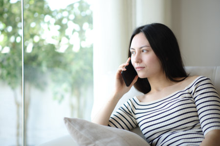 Asian woman talking on phone sitting on a sofa at homeの写真素材
