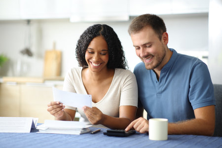 Happy interracial couple accounting in the kitchen at homeの写真素材
