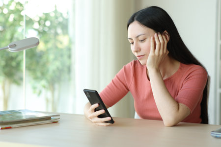 Asian woman checking phone content on a desk at homeの写真素材