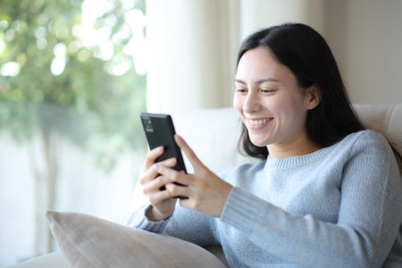 Happy asian woman using smart phone sitting on a sofa at homeの写真素材