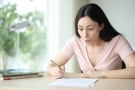 Amazed asian woman reading contract ready to sign on a desk at homeの写真素材