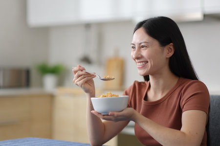 Happy asian woman eating cereals in the kitchen at homeの写真素材