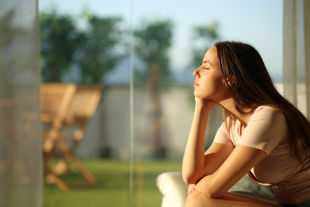 Woman relaxing and resting closing eyes at sunset sitting on a couch at home beside a windowの写真素材