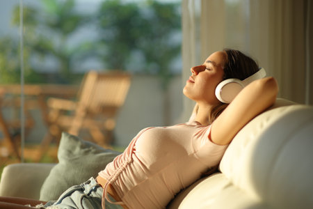 Profile of a woman relaxing at sunset wearing headphone listening audio sitting on a couch at homeの写真素材