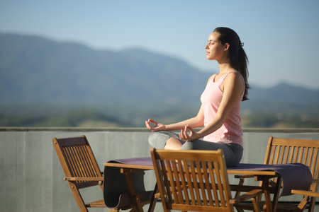 Side view portrait of a woman doing yoga on a table in a tarrace at homeの写真素材