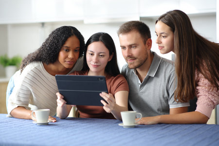 Four interracial friends checking tablet content in the kitchen at homeの写真素材