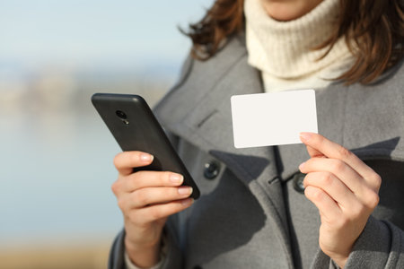 Close up of a woman hand holding blank credit card and smart phone in winter on the beachの写真素材