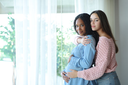 Black pregnant lesbian woman and her wife looking at camera at homeの写真素材